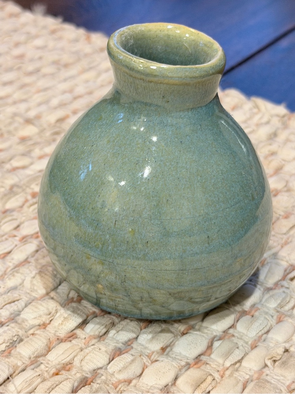 Signed ceramic bud vase features a rounded shape and a textured green glaze